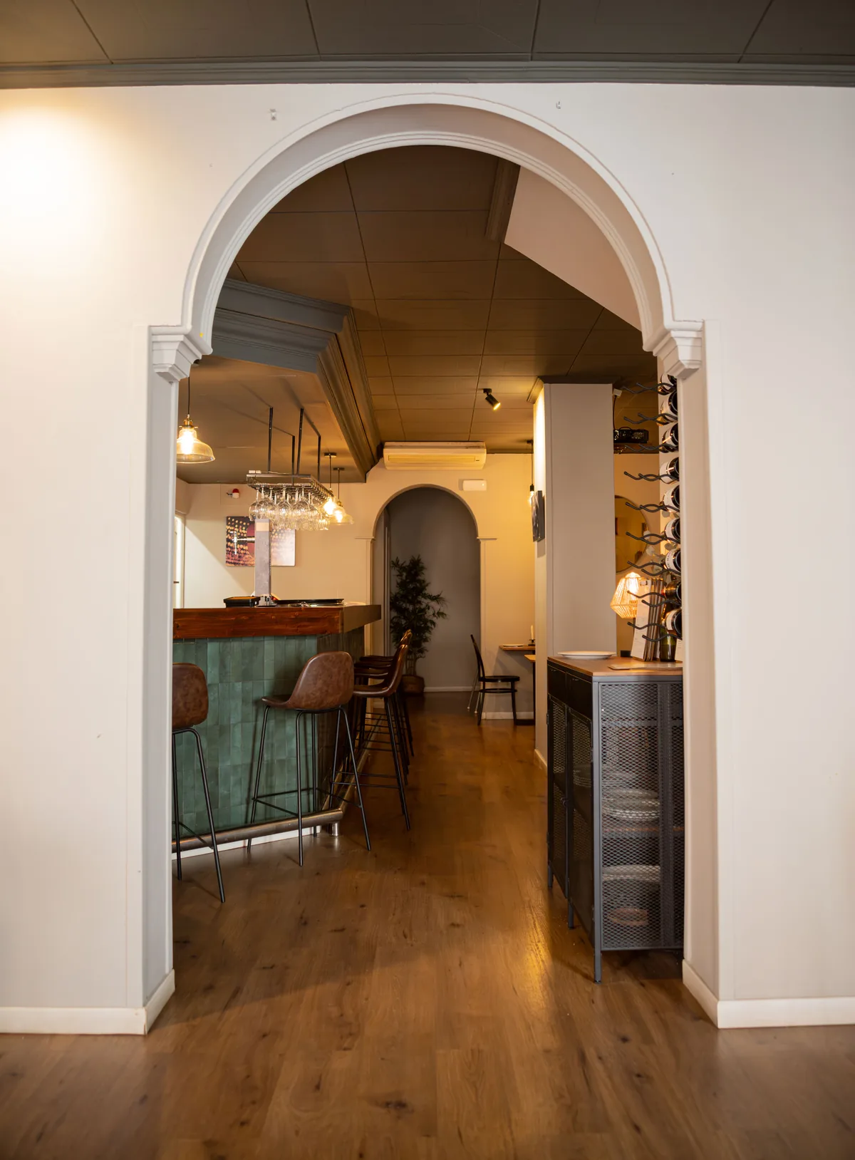 Restaurant interior seen through a white arch, with a green tiled bar and leather stools on an oak floor