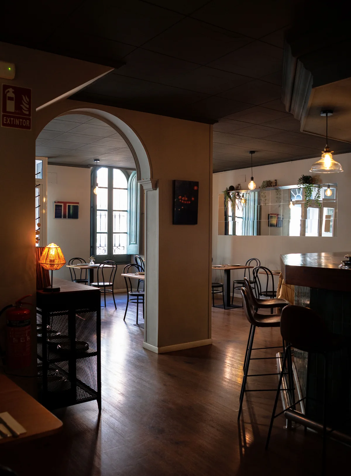 Dimly lit dining room with bentwood chairs, pendant lamps and a tall window at the back