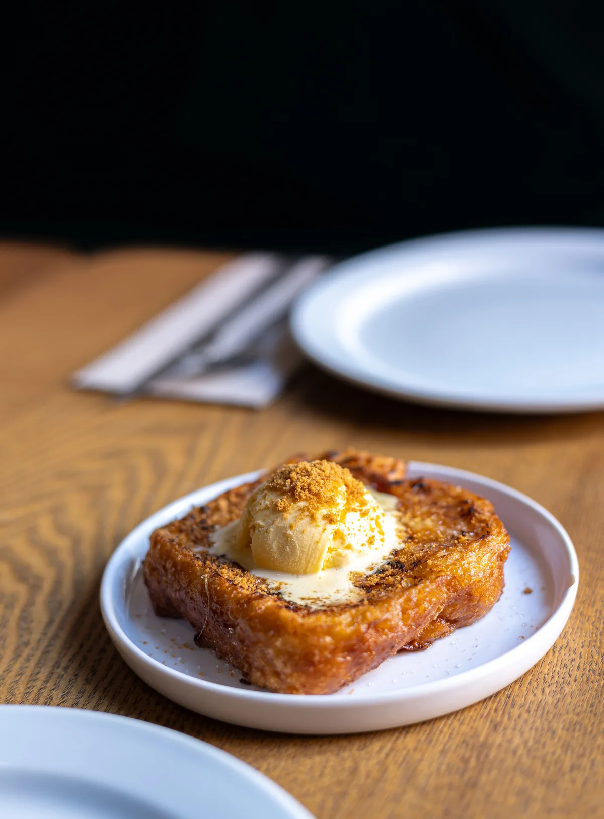Caramelised brioche toast topped with a scoop of ice cream on a small white plate