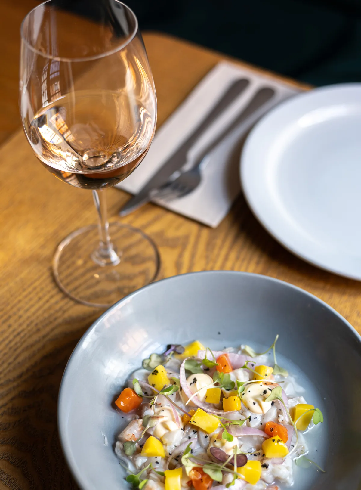 Ceviche with mango and red onion in a grey bowl, next to a glass of white wine