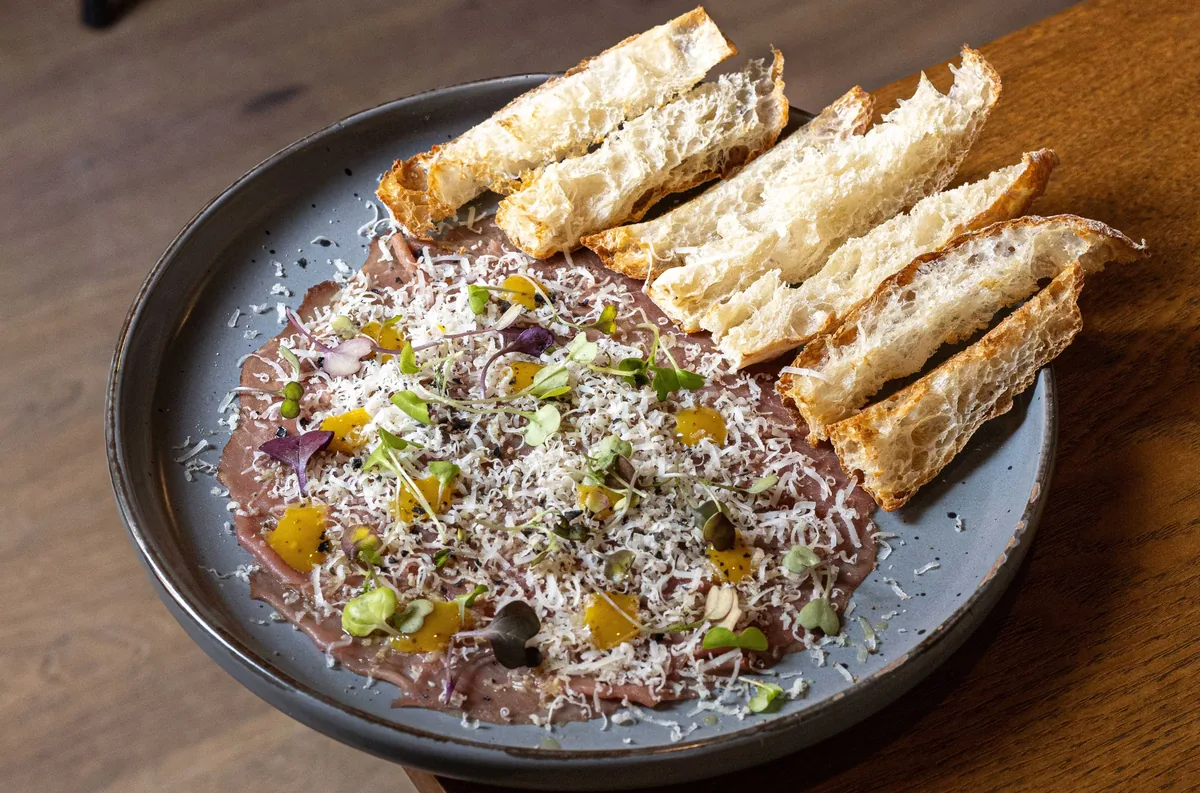 Beef carpaccio under grated cheese and herbs, with slices of toasted bread
