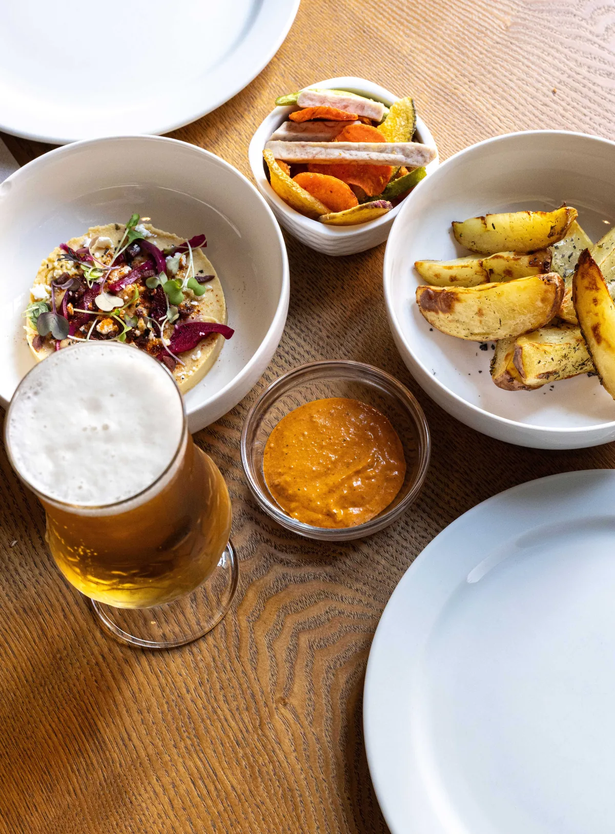 Table shot from above: a tostada, roast potatoes, grilled vegetables, romesco and a glass of beer