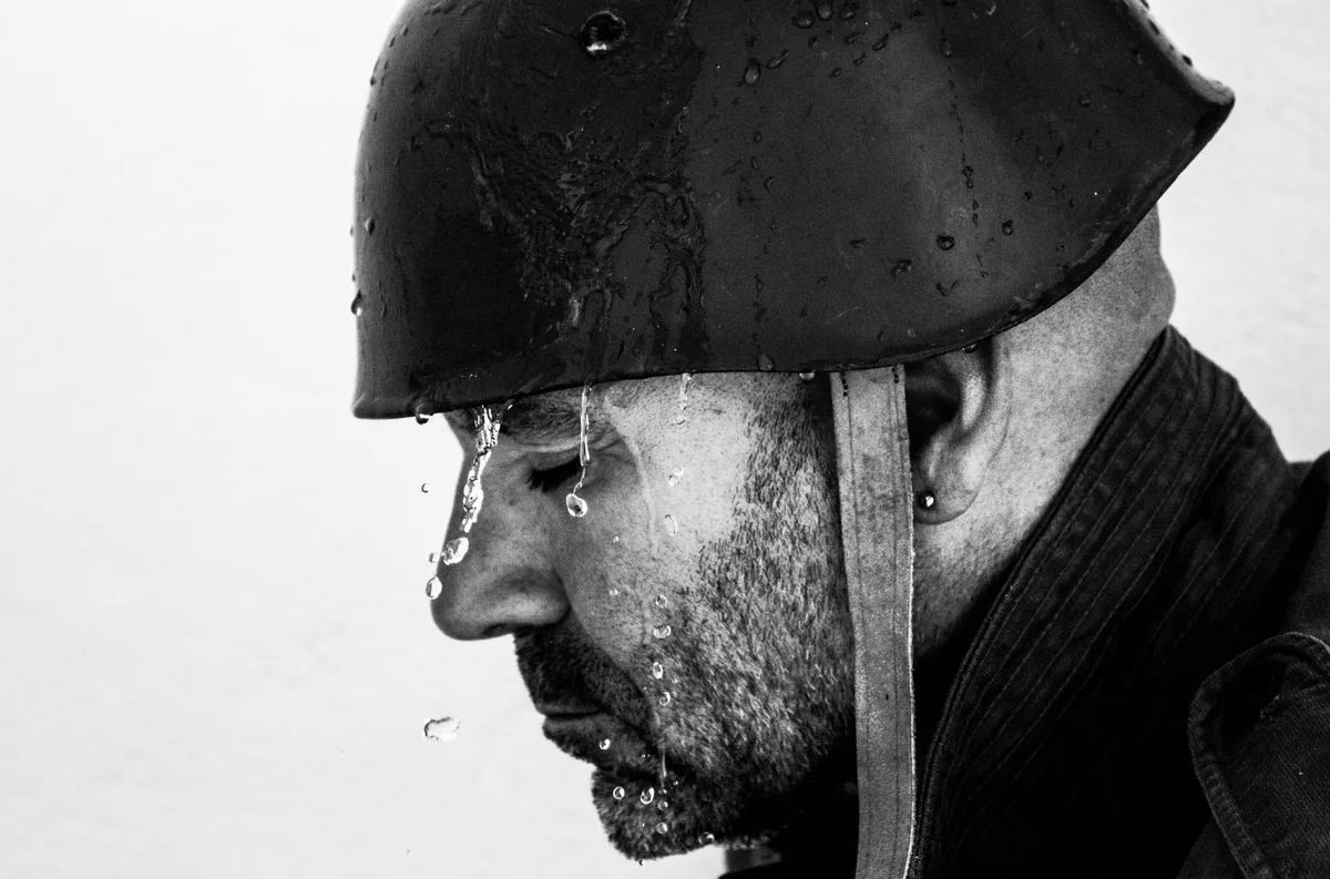 Man in a wet steel helmet in profile, water running down his face and beard
