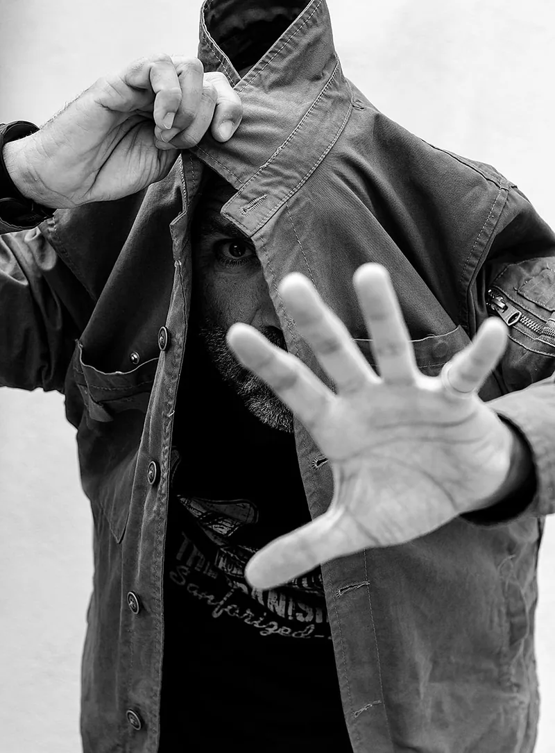 Man holding an open palm towards the lens and pulling his jacket collar up over his face
