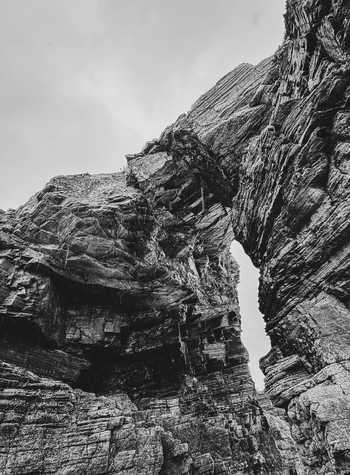 Layered sea cliff photographed from below, a narrow gap of sky splitting the rock