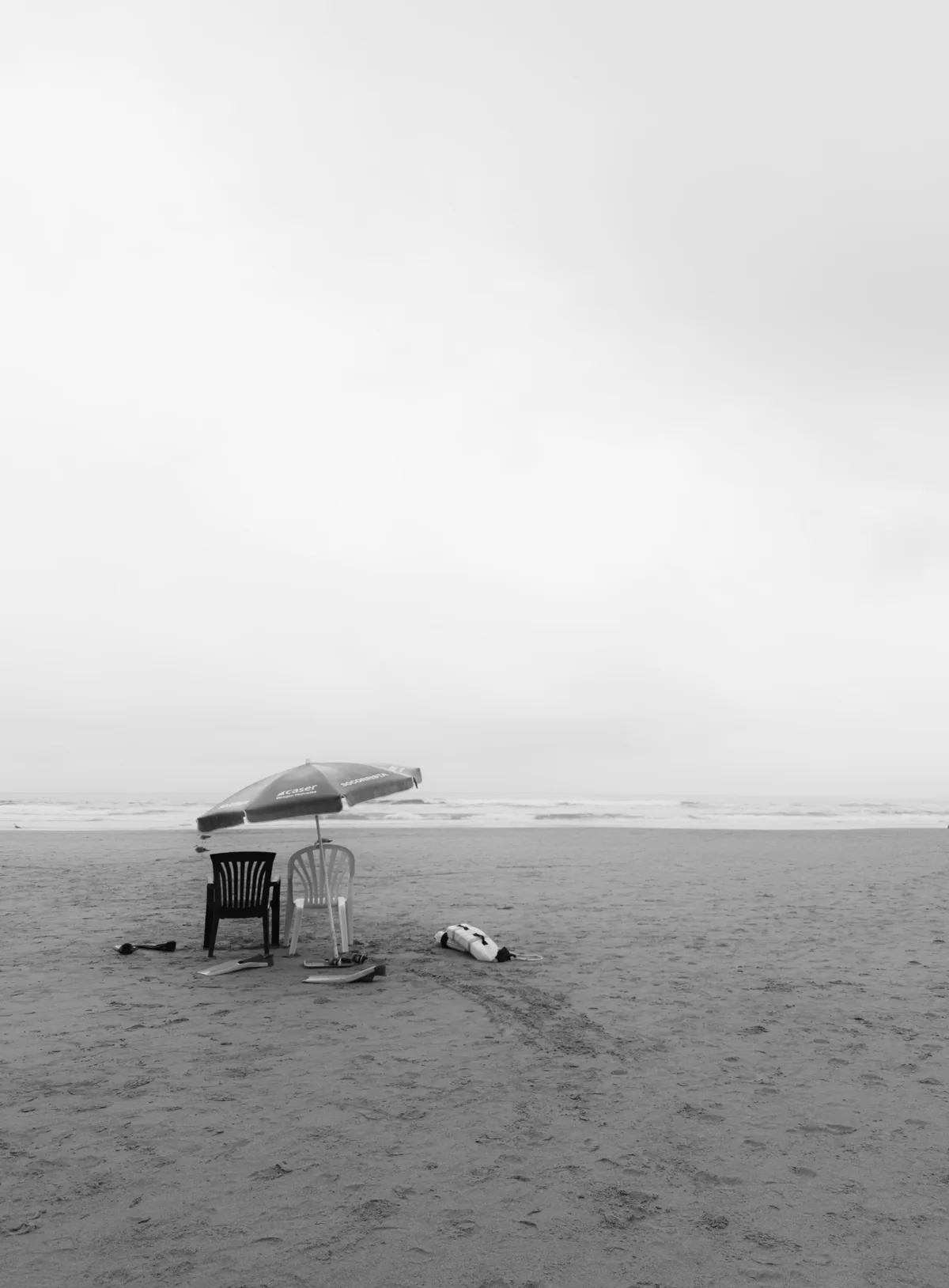Deserted beach under an overcast sky, a single parasol and two chairs left on the sand
