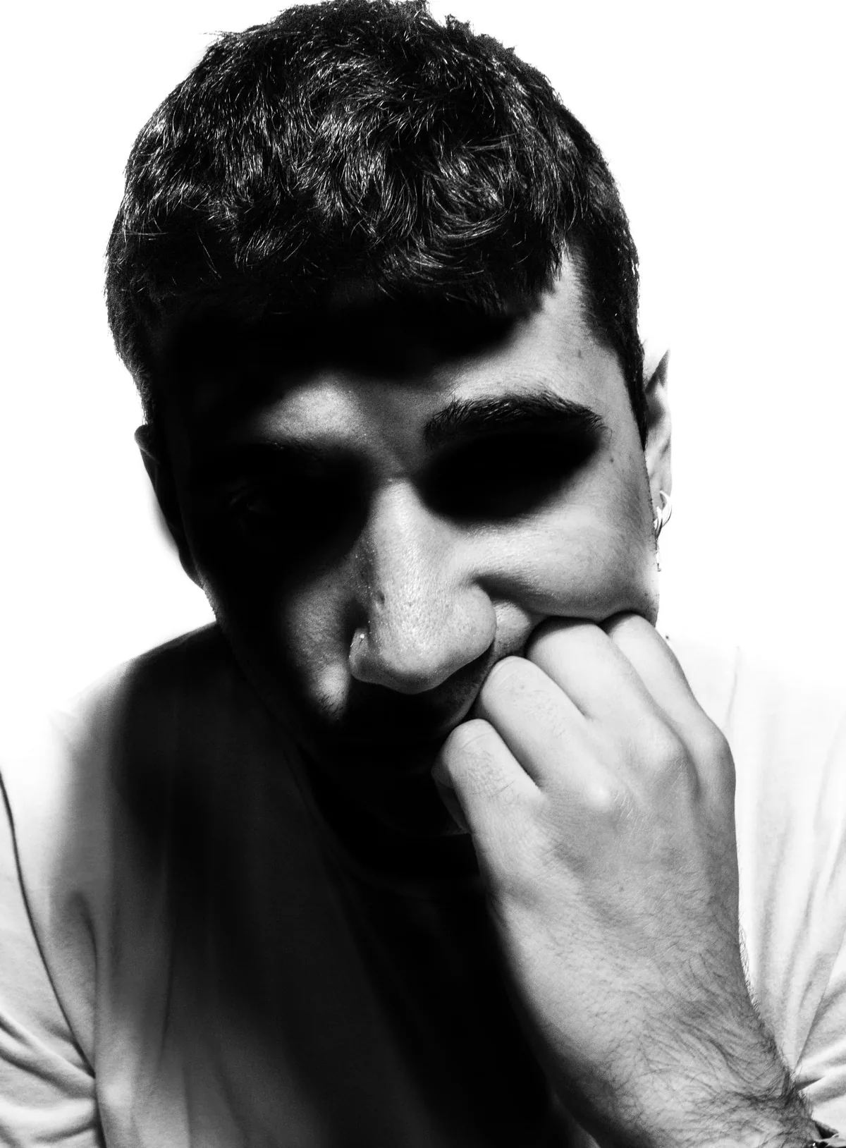 Young man with his head lowered and a hand at his mouth, a hard shadow cutting across his face