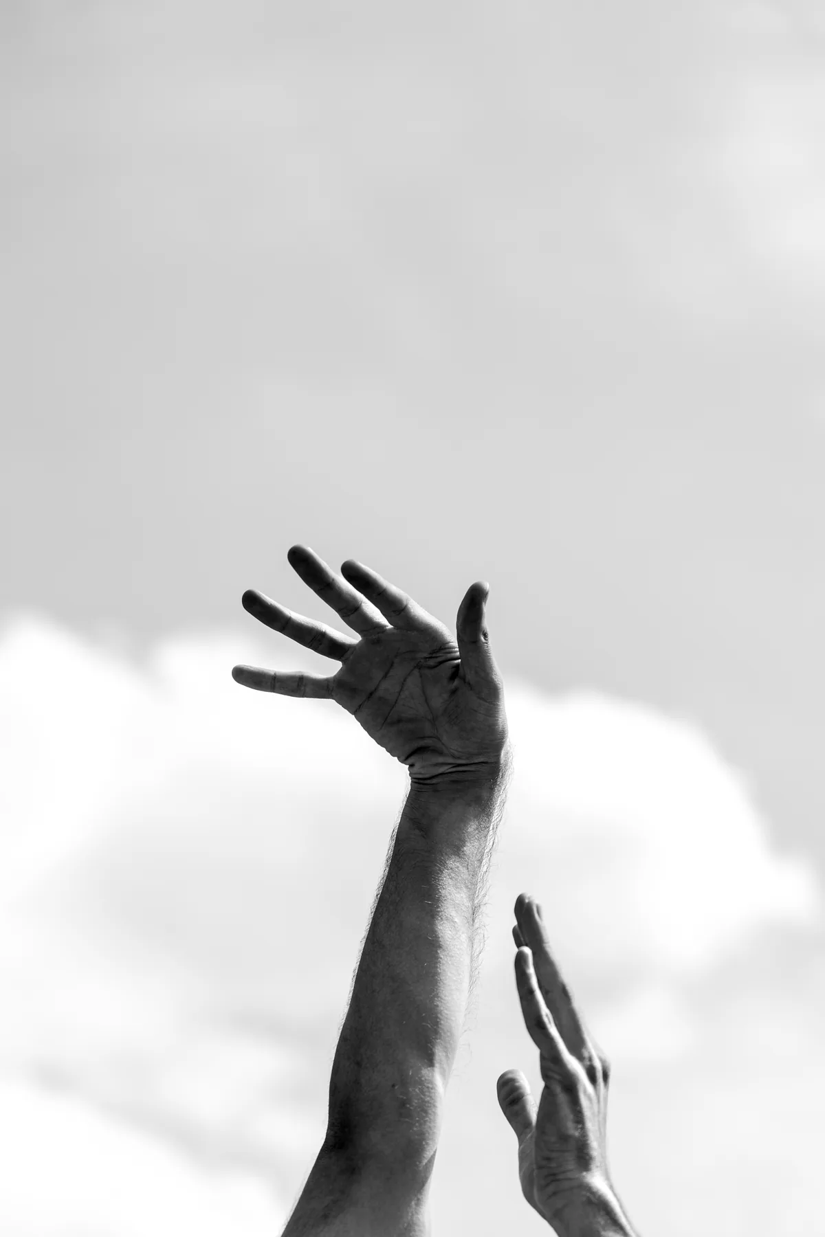 Two hands raised open against a bright, cloudy sky